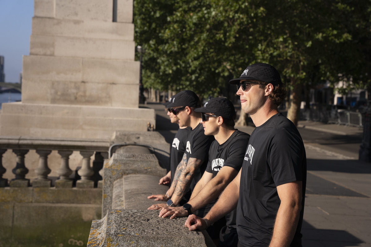 Group of runners in black kit resting against a river wall after a long road run in London