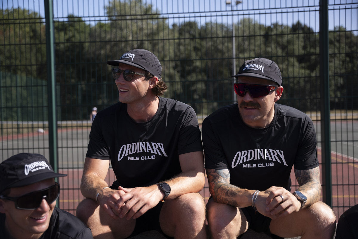 Two Ordinary Mile Club runners sitting side by side on a track bench, relaxed after a slow beginner run